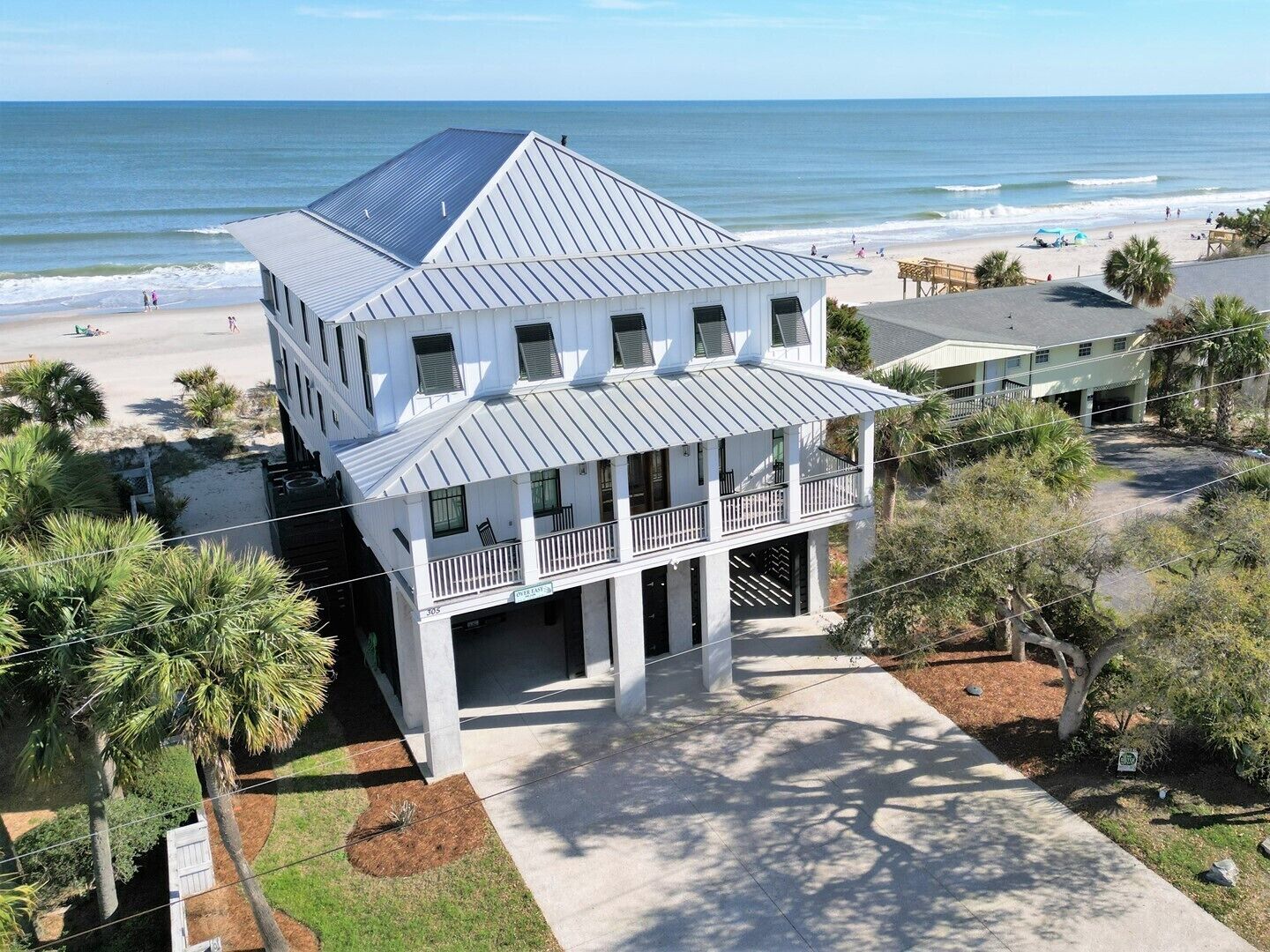 A two-story beachfront house with a balcony, a covered porch, and a view of the ocean.