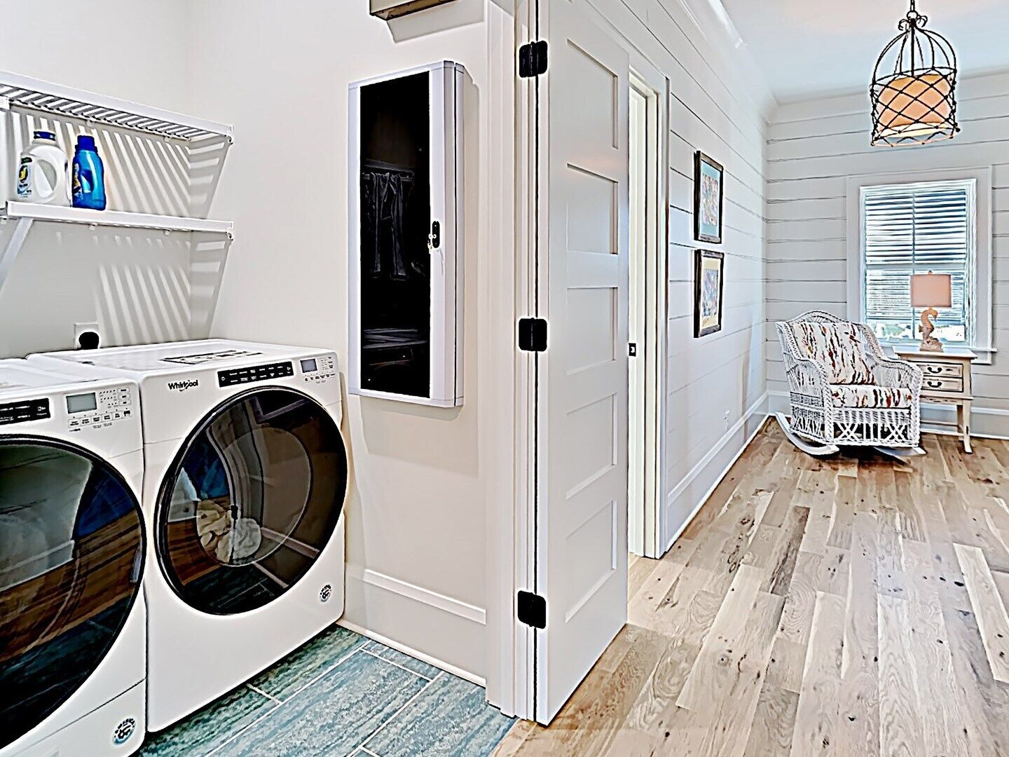 A laundry room with two front-loading washers and dryers, a shelf with laundry supplies, and a door leading to another room.
