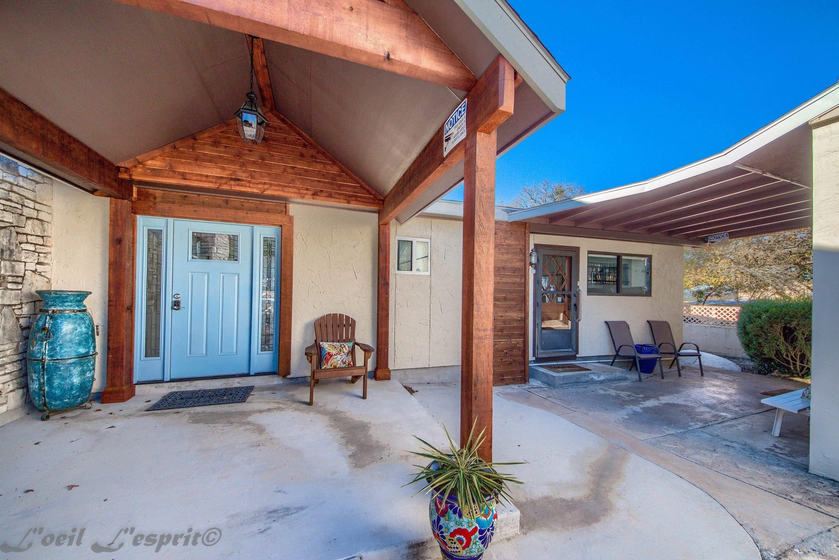 A covered porch with a blue door, a wooden chair, and a potted plant.