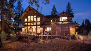 A large log cabin with multiple windows and a deck, surrounded by trees.