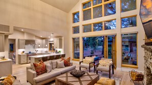 A spacious living area with a large sofa, coffee table, and seating area. There is a kitchen in the background with a dining area.