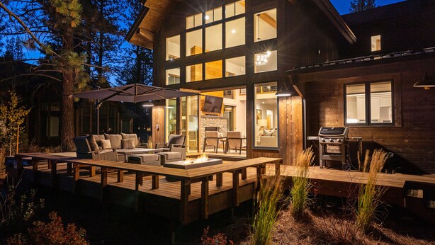 A wooden house with a deck, outdoor seating, and a fireplace.