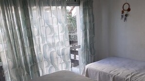 Ein Zimmer mit zwei Betten, einem Fenster mit gemusterten Vorhängen und einem Traumfänger an der Wand.
