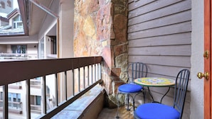A balcony with a stone wall, a small round table with a colorful tablecloth, and two blue cushioned chairs. - Luxurious 1br+loft - Ski-in/ski-out Access To Beaver Creek 1 Bedroom Condo by RedAwning (Avon)
