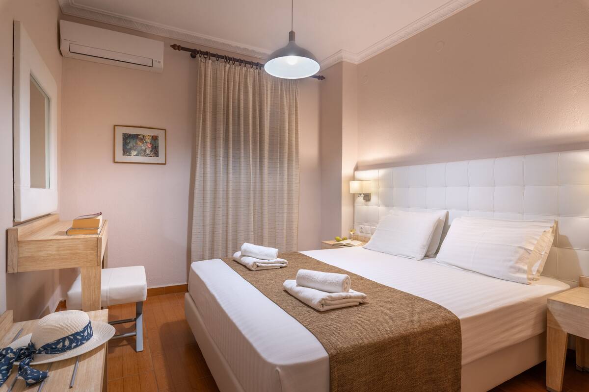 A hotel room with a bed, bedside table, lamp, and a window with curtains.
