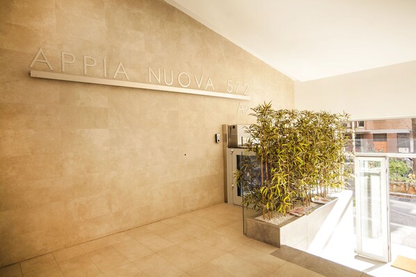 A modern reception area with a sign reading "APPIA NUOVA 572" and a glass door leading outside.