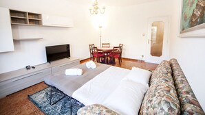 A modern hotel room with a bed, a sofa, a TV, a chandelier, and a dining area. - Appia Near Underground Station (Roma)