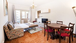 A compact room with a bed, a dining table with chairs, a TV, and a chandelier. - Appia Near Underground Station (Roma)