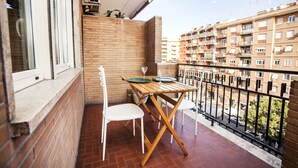A balcony with a wooden table and two white chairs, a brick wall, and a view of a residential building. - Appia Near Underground Station (Roma)