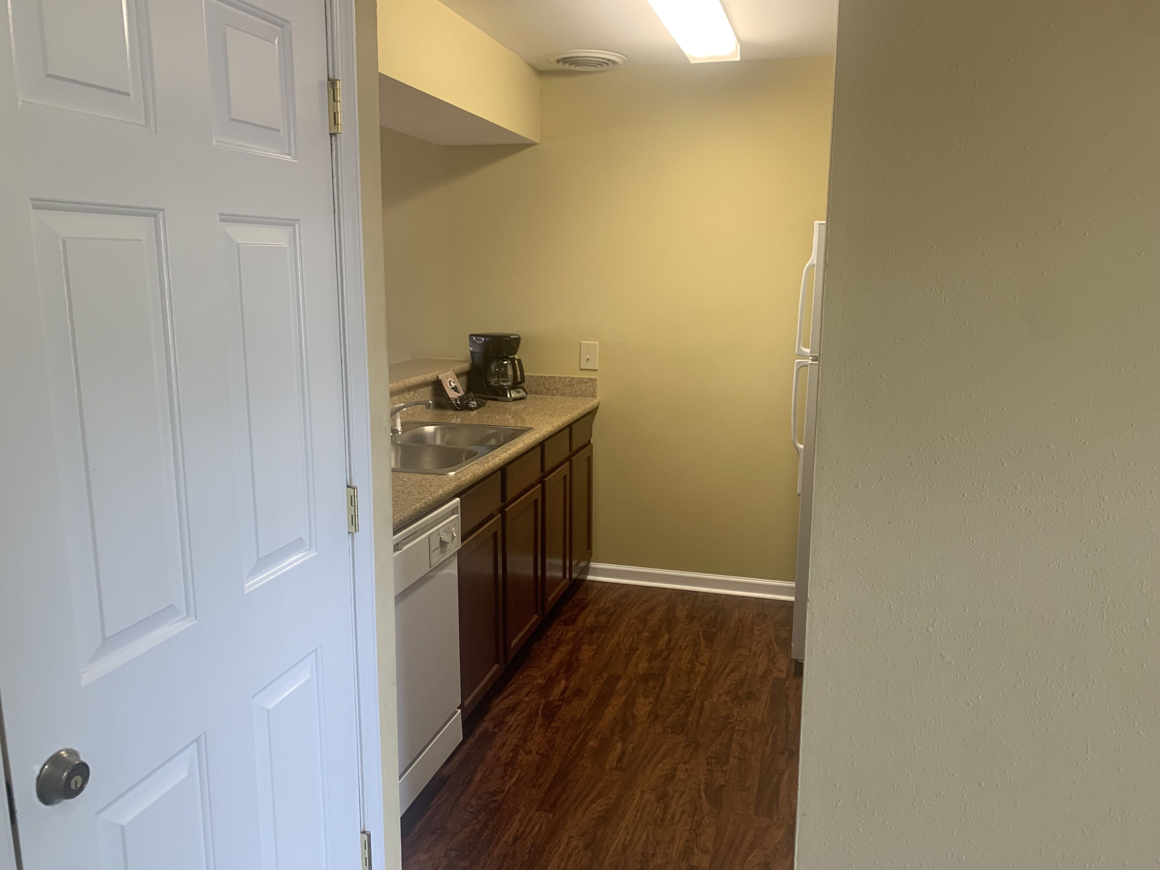 A narrow kitchen with a dishwasher, a coffee maker, and a refrigerator.