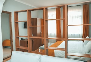 A hotel room with a wooden wardrobe, a bed with white bedding, a sofa, and a small table with a telephone. - Palm Hotel (Batumi)