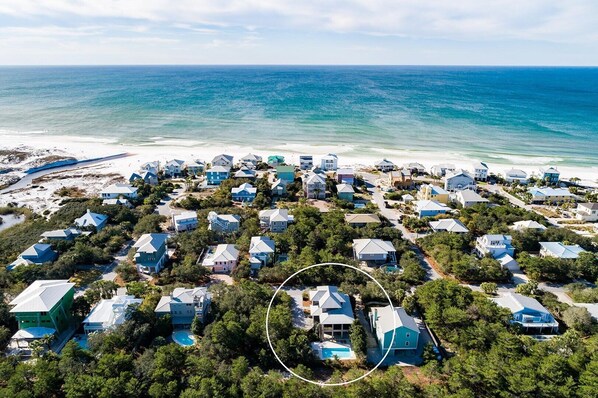 An aerial view of a coastal residential area with houses, a beach, and a clear view of the ocean.