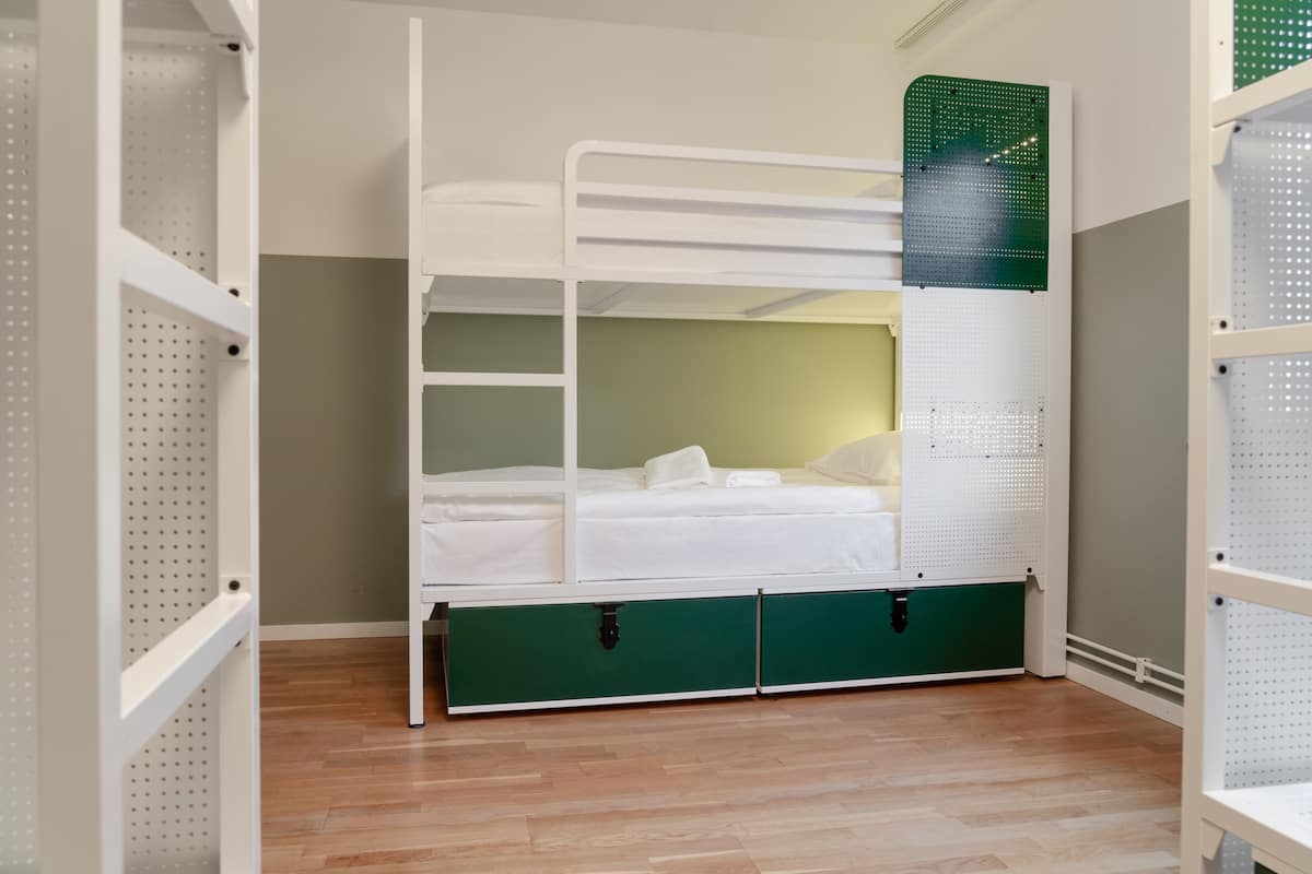 A bunk bed with a green storage compartment underneath, white metal railings, and a pegboard wall.