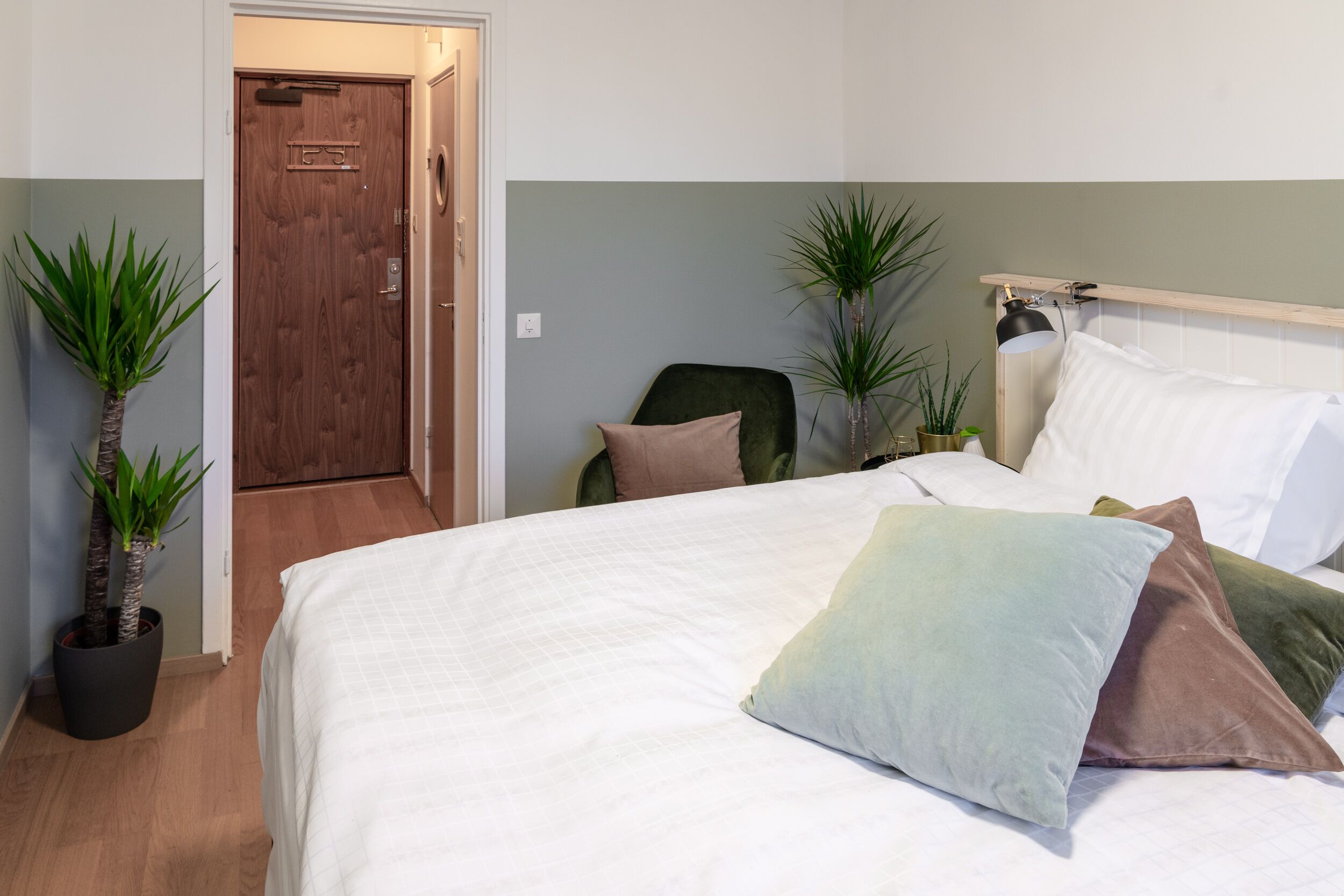 Una camera da letto con un letto, cuscini, una sedia e due piante in vaso.