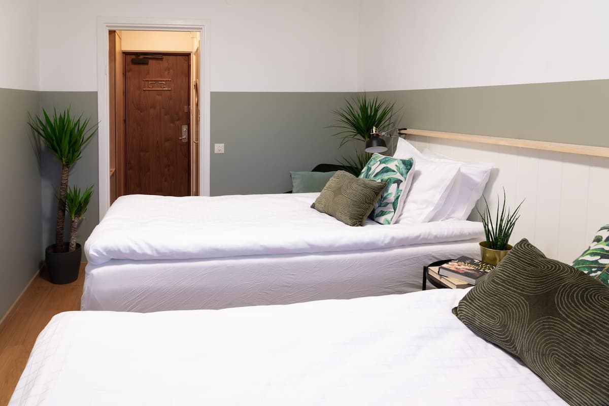 A bedroom with two beds, a wooden door, and potted plants.