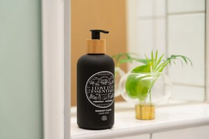 Una botella negra de jabón para manos con bomba de madera sobre un estante blanco.