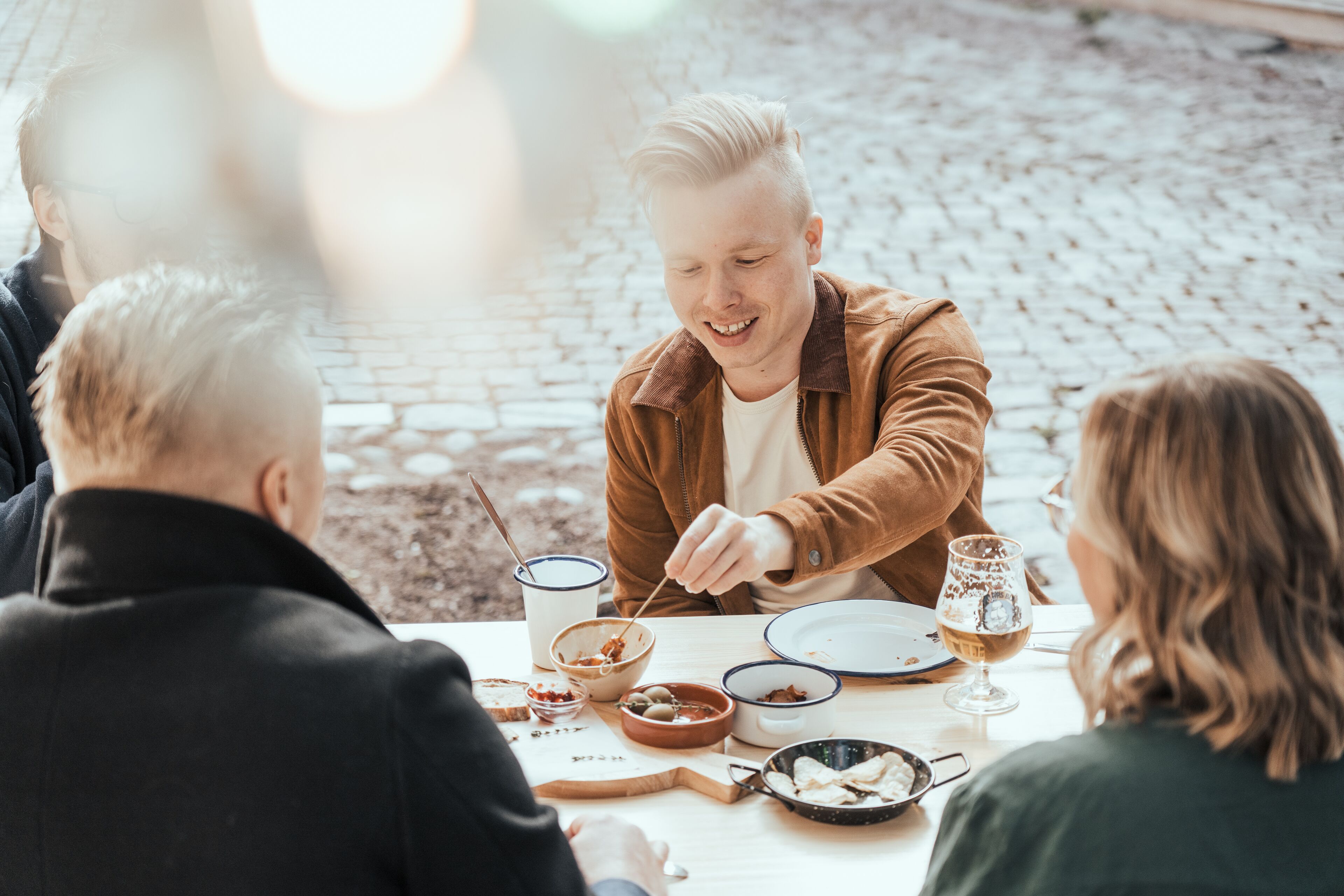 Un grupo de personas cenando en una mesa al aire libre, con diferentes platos y bebidas.