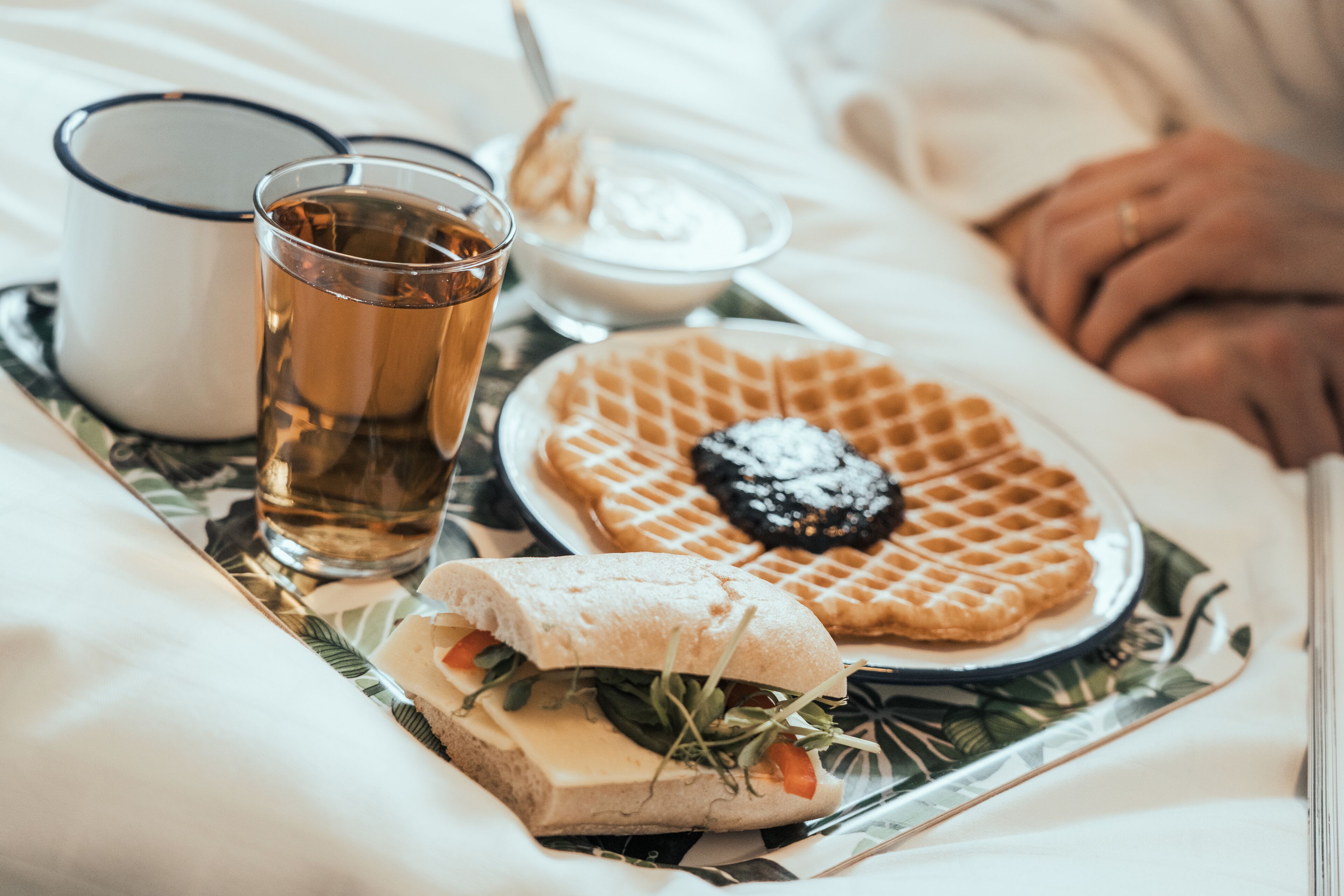 Una bandeja con un sándwich, un gofre, una taza de té y un tazón de yogur sobre una base.