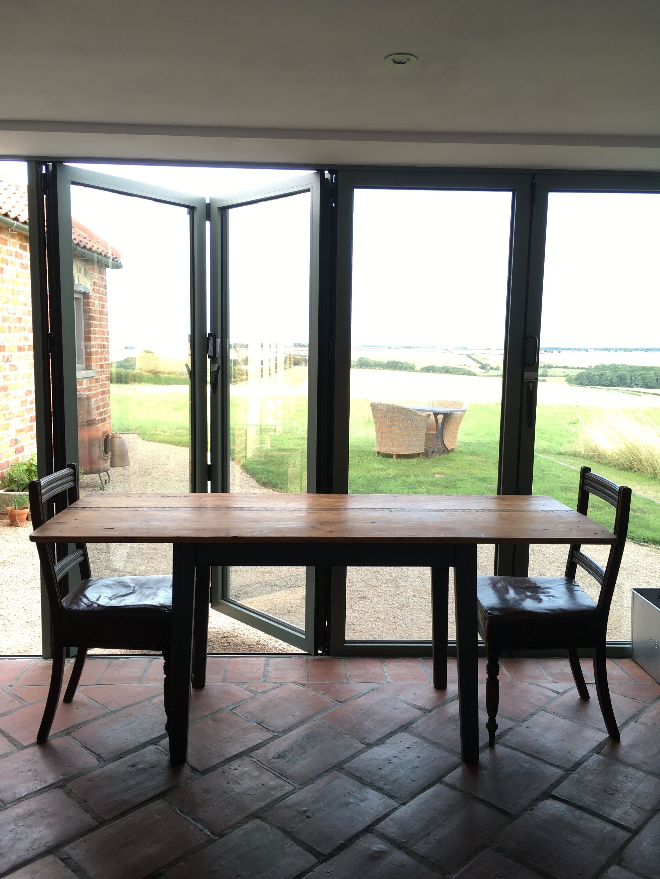 A dining area with a wooden table and two chairs, large glass doors leading to a garden view.