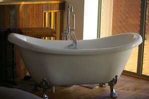Una bañera independiente en una habitación con suelo de madera y un ventanal grande.