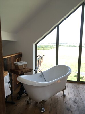 Un baño con bañera independiente, suelo de madera y un amplio ventanal con vistas al exterior.