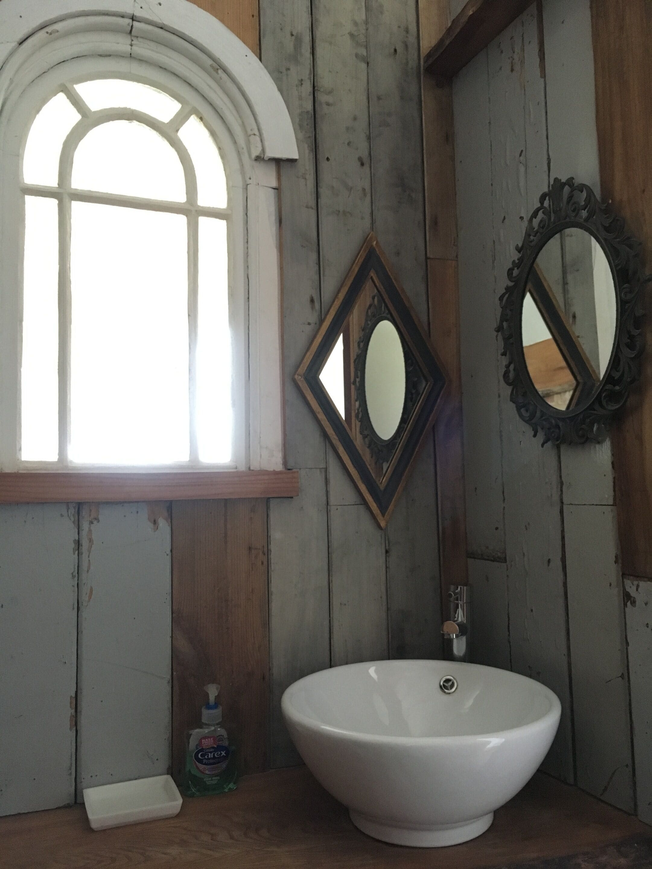 A bathroom with a white sink, a window with a white frame, and two mirrors on the wall.