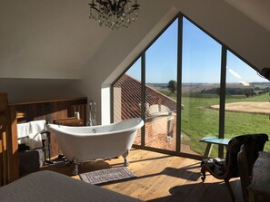 Ein geräumiges Zimmer mit einer großen Badewanne, Holzböden und Blick auf die Landschaft durch große Fenster.