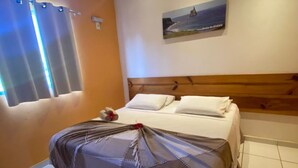A hotel room with a bed, a headboard, a painting on the wall, and a window with curtains.