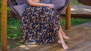 A person sitting on a wicker swing chair in an outdoor setting with a wooden deck and greenery in the background.