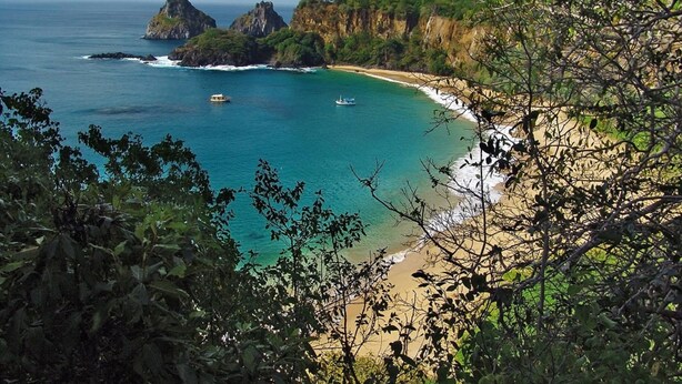 A coastal landscape with a beach, rocky cliffs, and boats on the water.