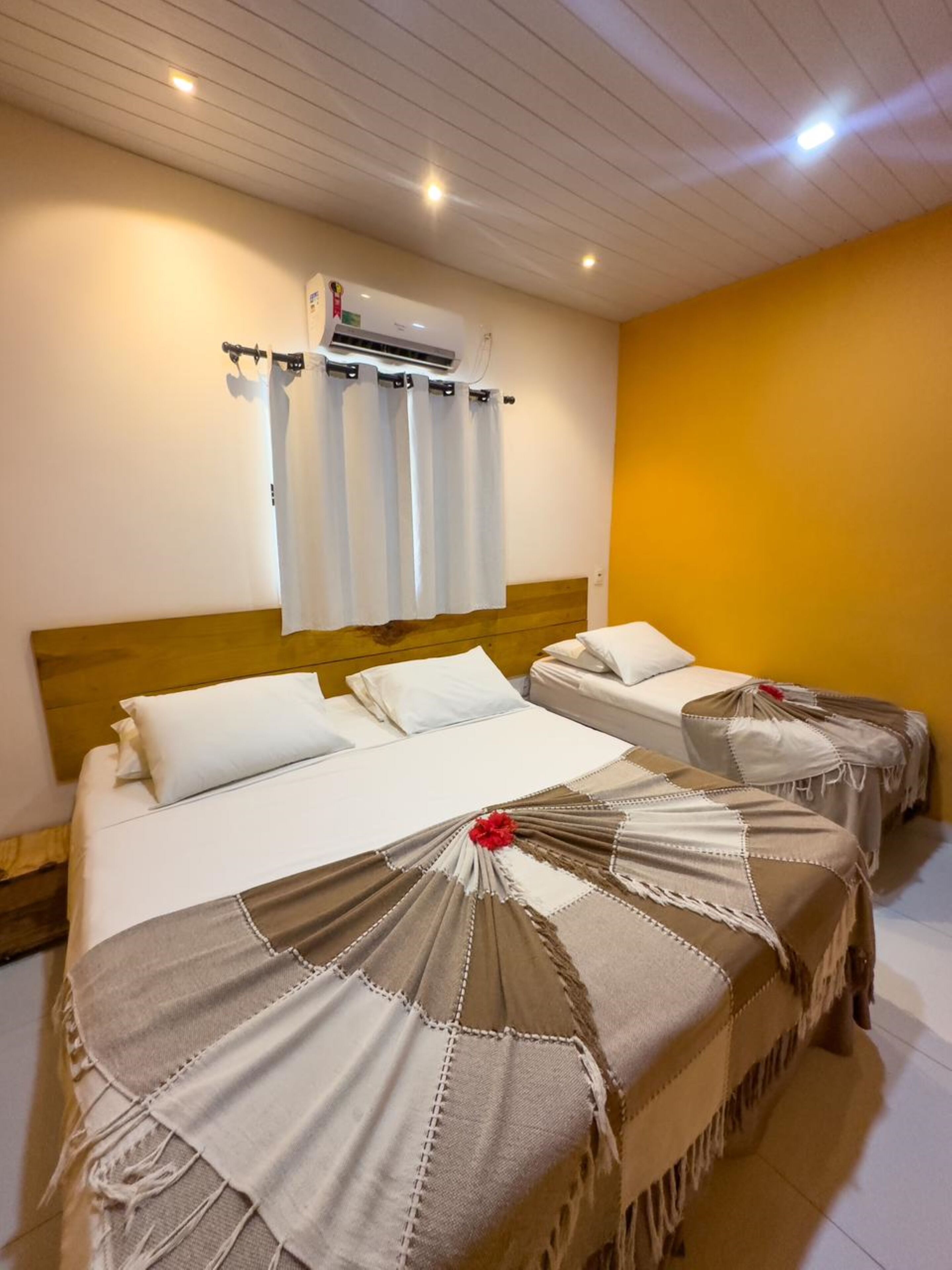Ein Hotelzimmer mit zwei Betten, einem Holzkopfende, einer Klimaanlage und einer gelben Wand.