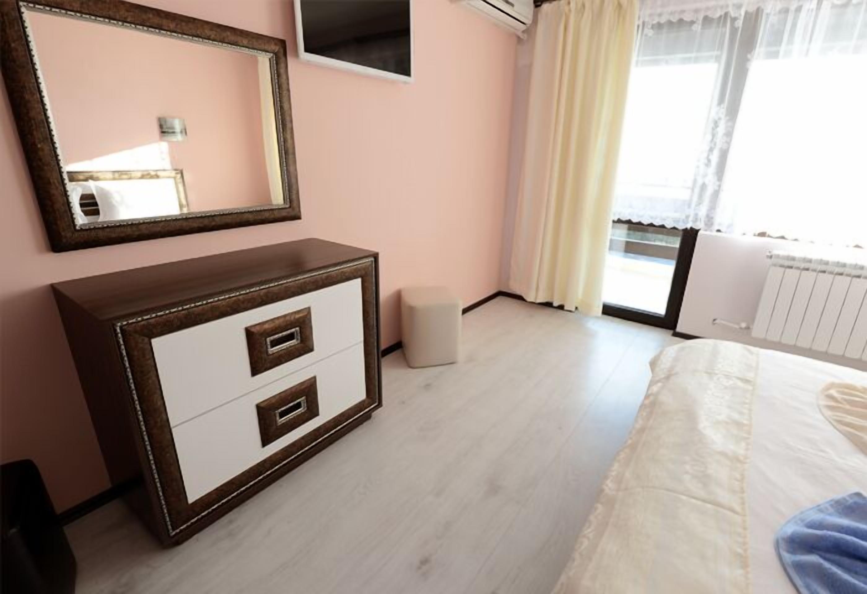 Un dormitorio con cama, cómoda, espejo y ventana con cortinas.