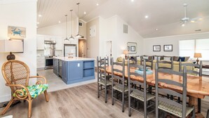 Une cuisine spacieuse équipée d’appareils modernes, un coin repas avec une table et des chaises en bois, et un coin salon confortable avec un canapé et un fauteuil.