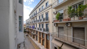 A narrow street with multi-story buildings, balconies with potted plants, and a clear sky. - Neoclassical Apartment near Syntagma - Plaka by GHH (Athens)