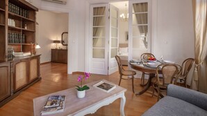 A living room with a wooden coffee table, a bookshelf, a dining area with a table set for two, and a doorway leading to another room. - Neoclassical Apartment near Syntagma - Plaka by GHH (Athens)