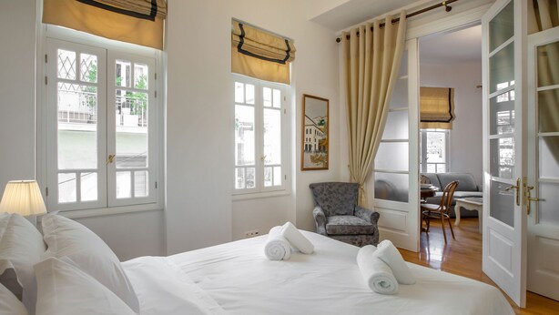 A hotel room with a large bed, a chair, a desk, and a view of the outside. - Neoclassical Apartment near Syntagma - Plaka by GHH (Athens)