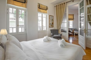 A hotel room with a large bed, a chair, a desk, and a view of the outside. - Neoclassical Apartment near Syntagma - Plaka by GHH (Athens)