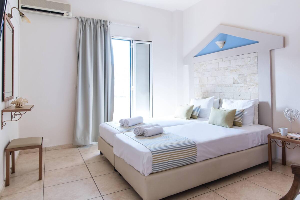 Hotelkamer met een groot bed, nachtkastje, stoel, raam met gordijnen en een wandairconditioner.