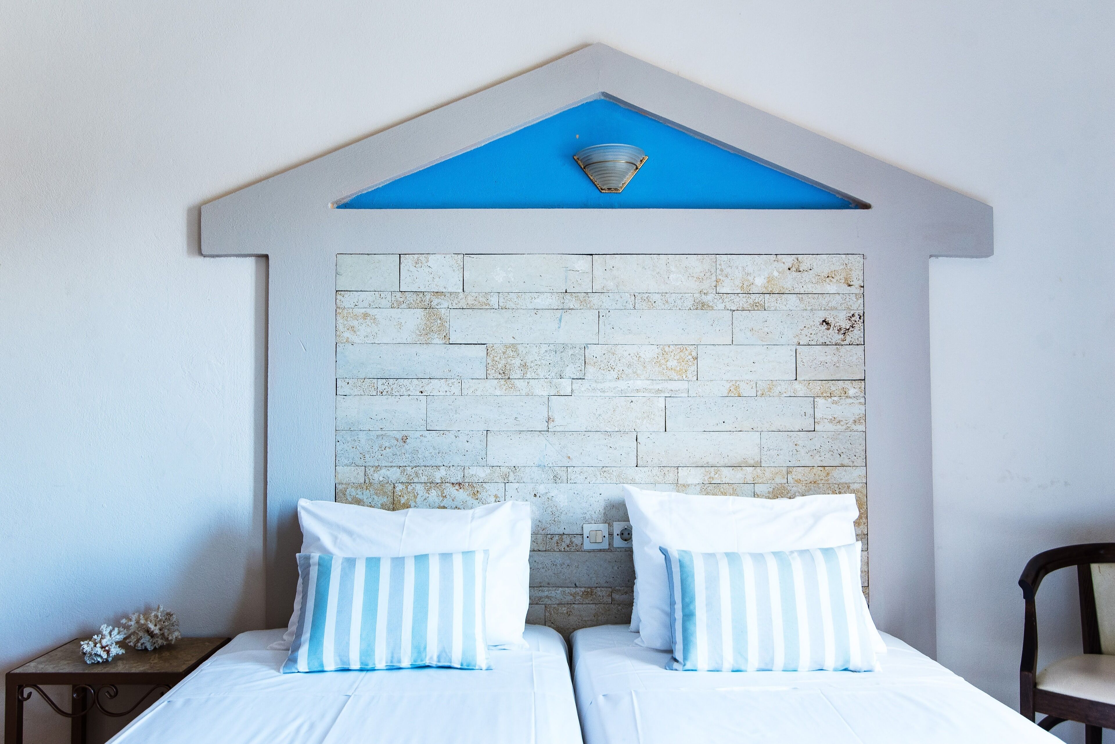 A bedroom with two beds, a brick-patterned headboard, and a blue accent wall.