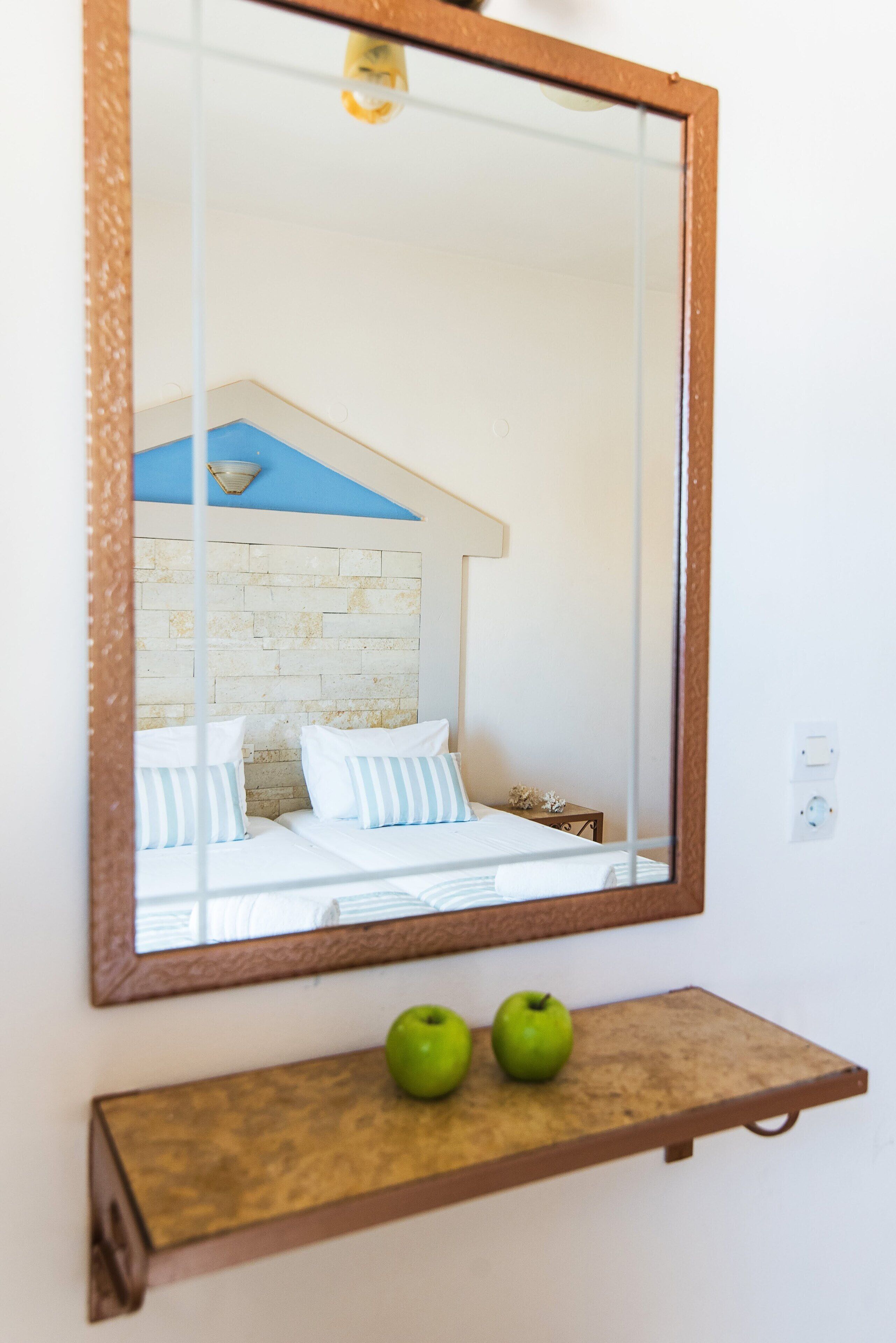 Quarto com cama, espelho e prateleira com maçãs.