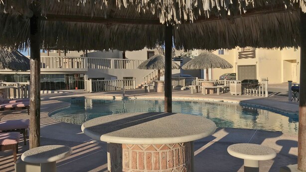 Un espace piscine agrémenté de parasols en chaume, de sièges et d’un bar.
