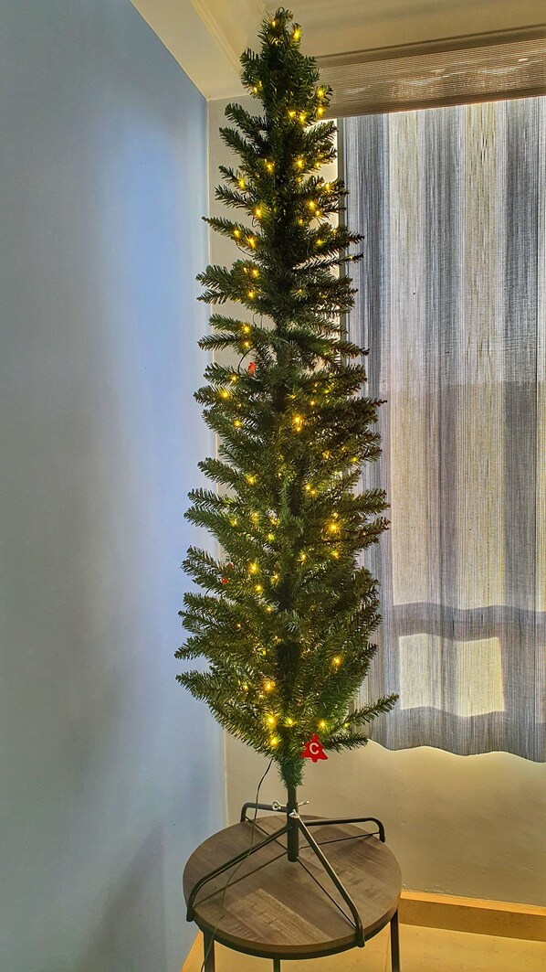 Een kerstboom met lichtjes op een ronde tafel in een kamer met een raam en gordijnen.