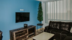 Un salon avec un téléviseur fixé au mur, un meuble de rangement en bois, un canapé en cuir noir et un petit sapin de Noël.