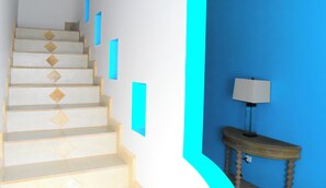 Un escalier orné d’un motif géométrique, un mur bleu et une lampe posée sur une table en bois.
