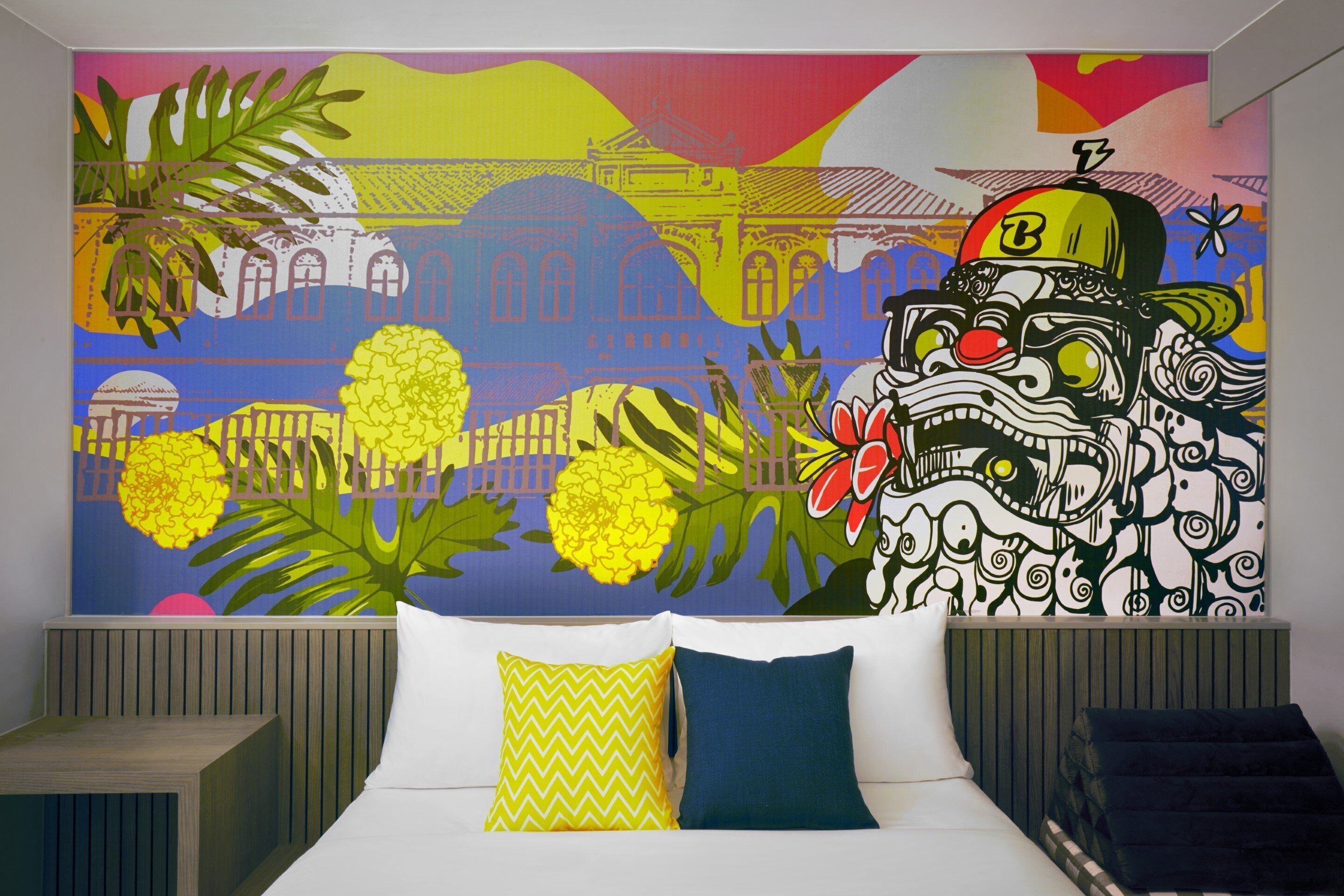A bedroom with a bed, two pillows, a colorful mural on the wall, and a nightstand.
