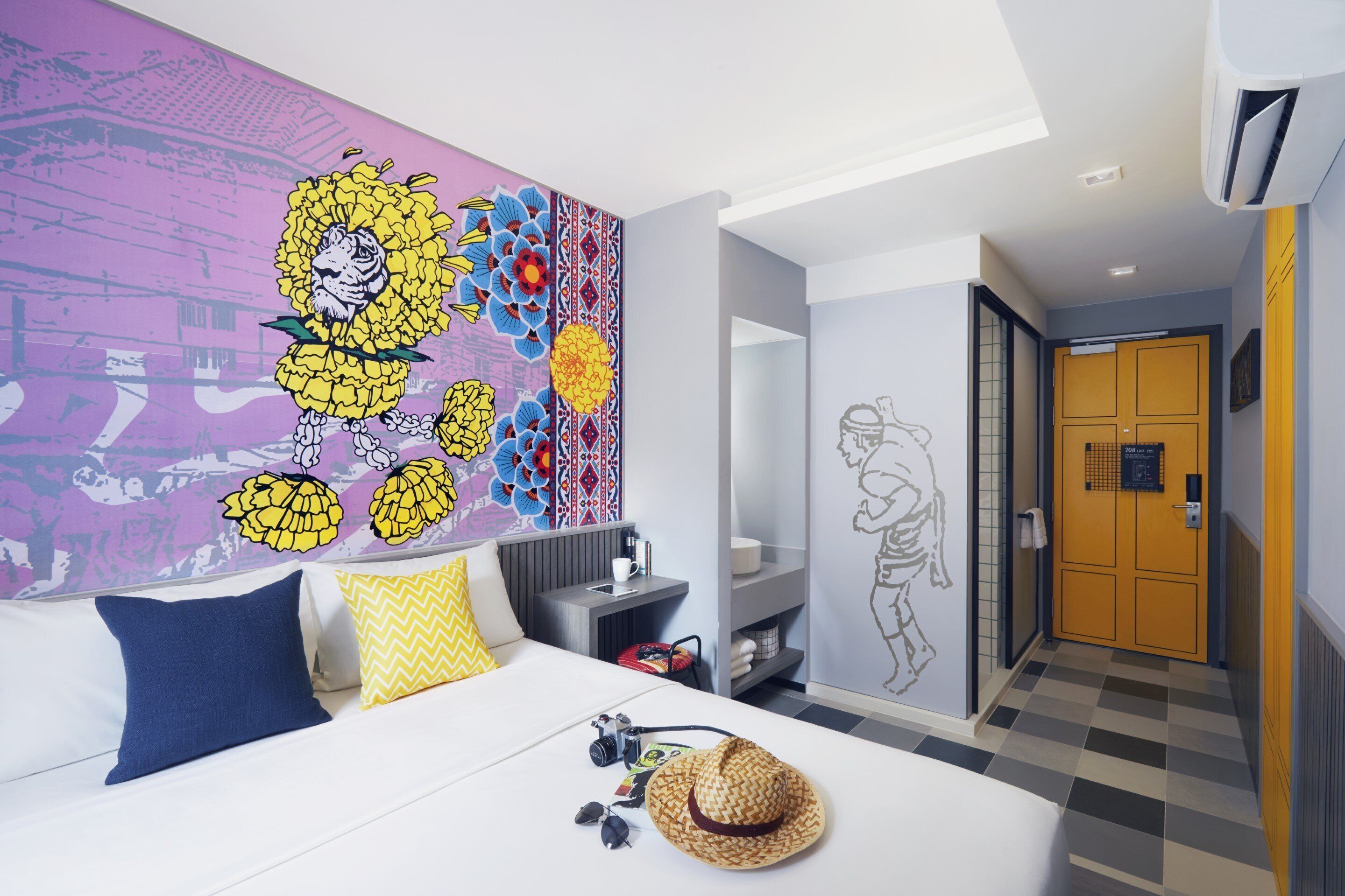 A modern hotel room with a large bed, a wall mural, a wardrobe, and a bathroom with a tiled floor.