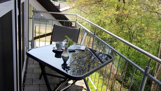 Un balcón con mesa y sillas, baranda y vista a árboles.