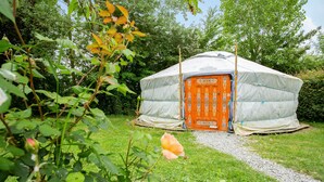 A yurt with a white and orange exterior, surrounded by greenery and a gravel path.