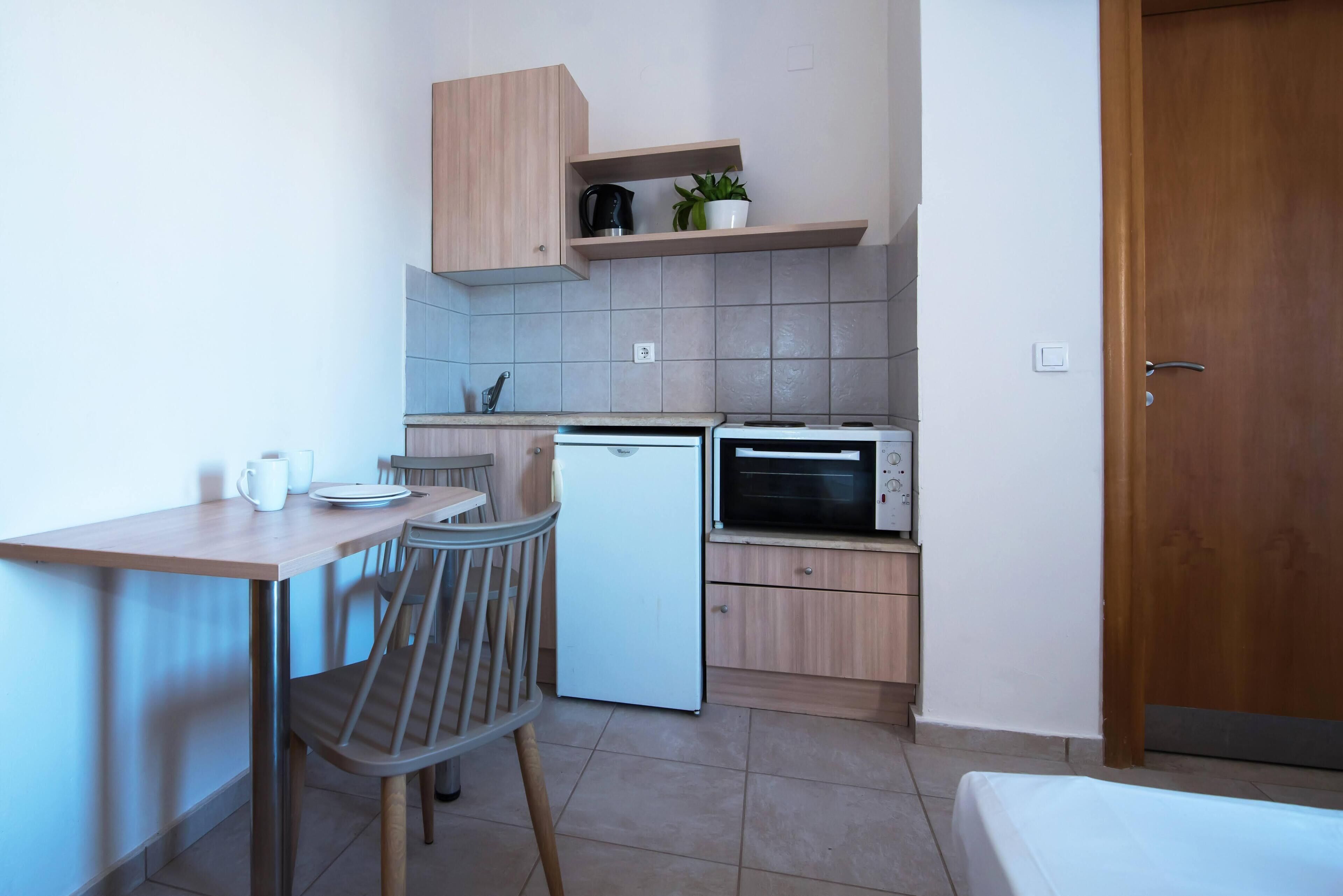 A compact kitchen with a dining area, a refrigerator, a microwave, and a wooden cabinet with a plant.