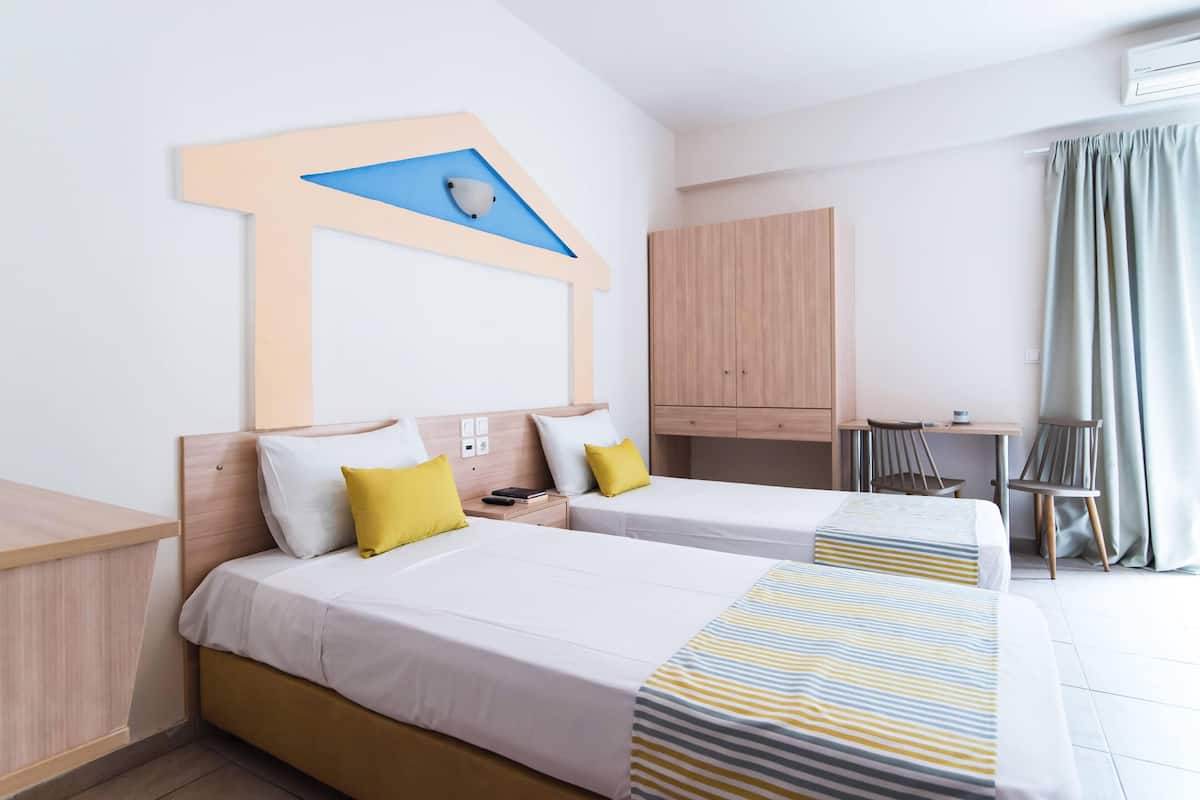 A hotel room with two beds, a desk, a wardrobe, and a bathroom.
